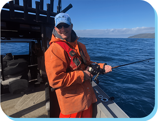 A man in an orange jacket is fishing on the boat.