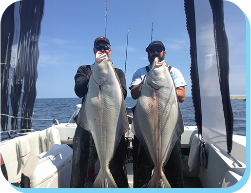 Two men holding up large fish on a boat.