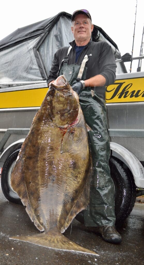 A man holding a large fish in front of a truck.