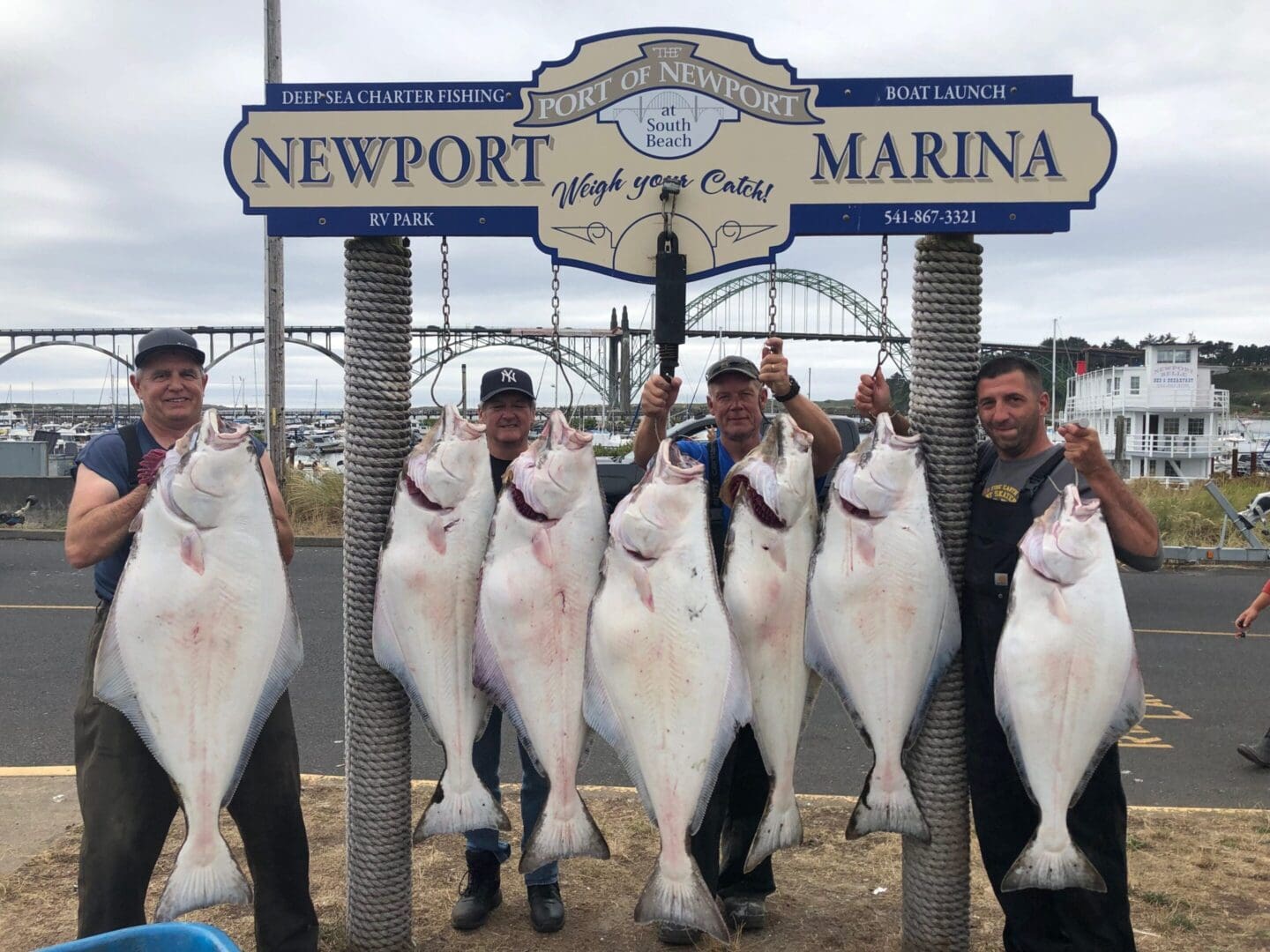 A group of men holding fish in front of a sign.