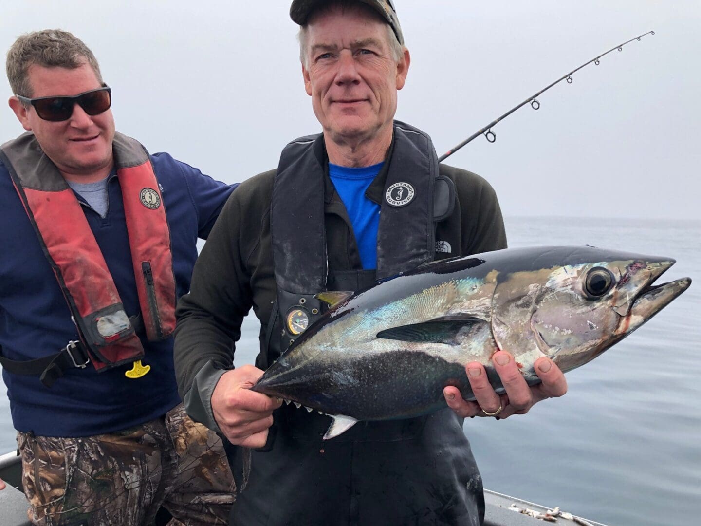 A man holding a fish while standing next to another man.